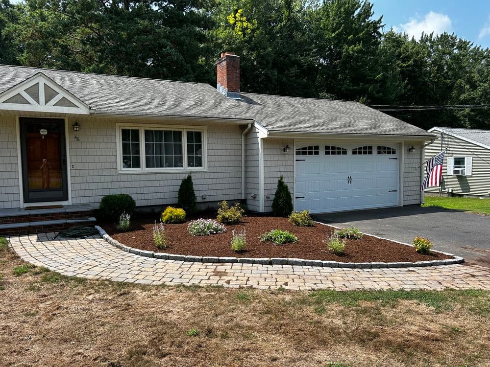 Single-story home with a paved driveway, landscaped garden, and American flag.