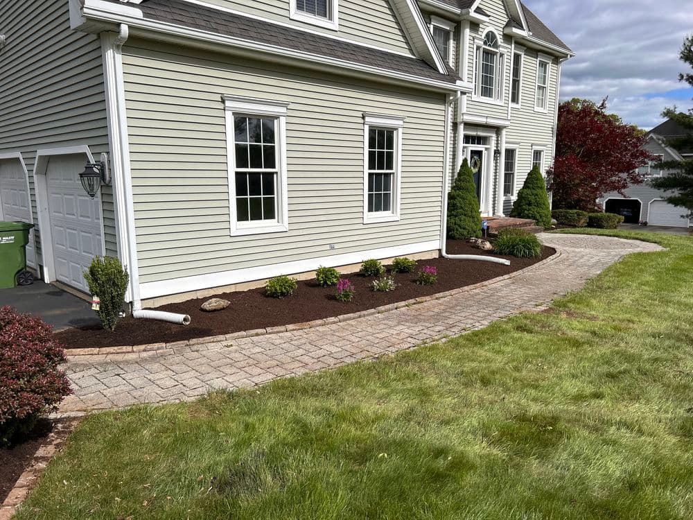 Well-landscaped home exterior with stone pathway, flowers, and manicured lawn.