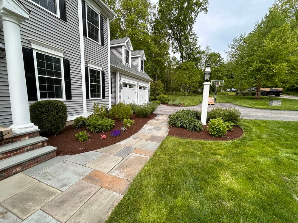 Walkway with stone pavers, landscaped gardens, and a home exterior in a suburban setting.